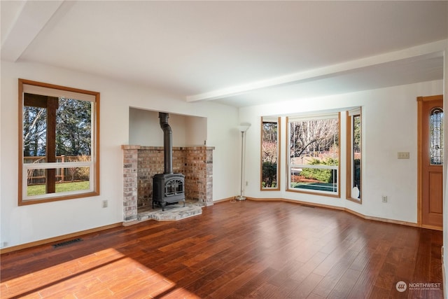 unfurnished living room featuring beam ceiling, wood-type flooring, and a wood stove