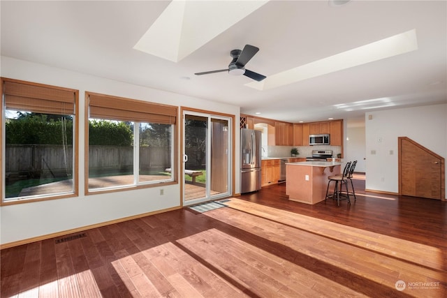 kitchen with appliances with stainless steel finishes, dark hardwood / wood-style flooring, a breakfast bar, and a kitchen island