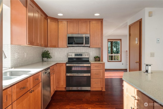 kitchen with appliances with stainless steel finishes, sink, backsplash, light stone counters, and dark wood-type flooring