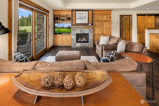 living room with built in shelves, dark hardwood / wood-style flooring, and a tiled fireplace