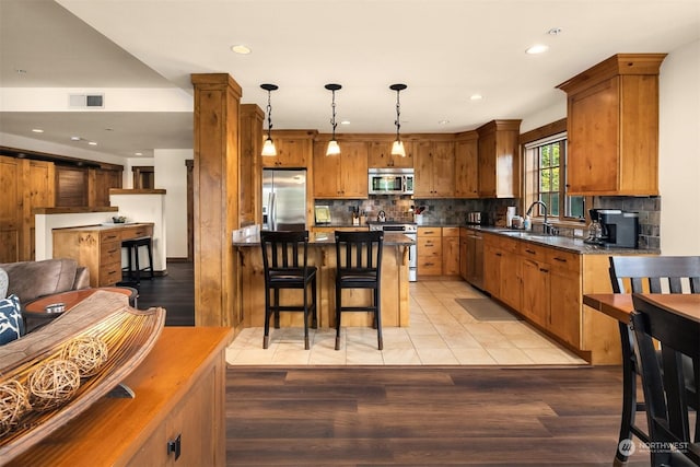 kitchen featuring appliances with stainless steel finishes, decorative light fixtures, sink, and light wood-type flooring