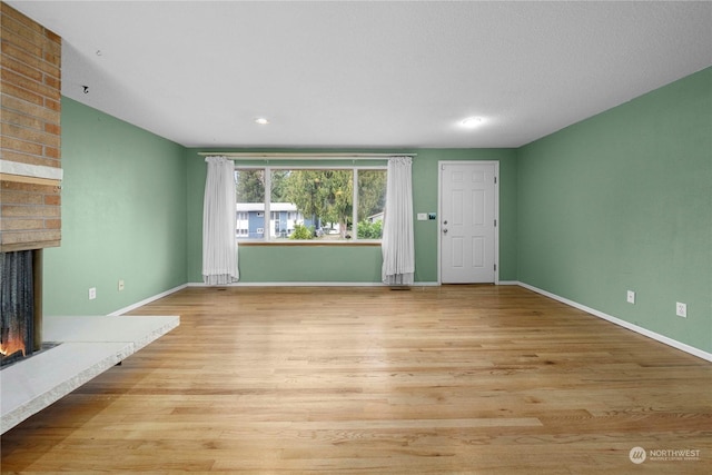 unfurnished living room with a brick fireplace and light hardwood / wood-style flooring