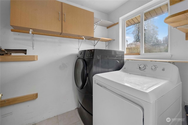 clothes washing area featuring light tile patterned floors, washing machine and clothes dryer, and cabinets