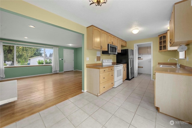 kitchen featuring appliances with stainless steel finishes, light tile patterned flooring, light brown cabinetry, a textured ceiling, and sink