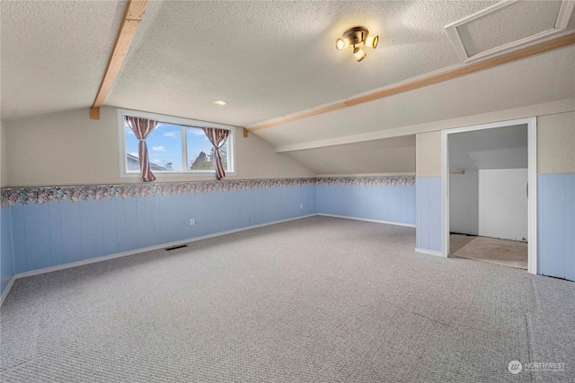 additional living space featuring a textured ceiling, carpet flooring, and vaulted ceiling with beams