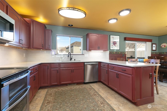 kitchen with appliances with stainless steel finishes, kitchen peninsula, a breakfast bar, sink, and tasteful backsplash