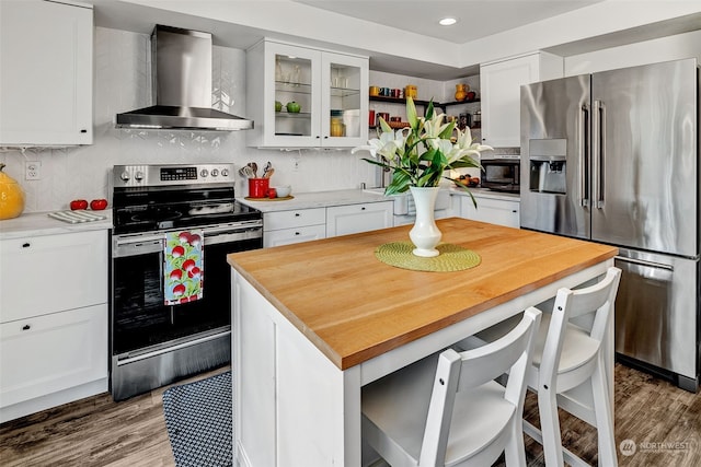 kitchen featuring appliances with stainless steel finishes, a center island, white cabinets, wall chimney range hood, and tasteful backsplash