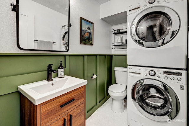 bathroom with toilet, tile patterned flooring, stacked washer and clothes dryer, and vanity