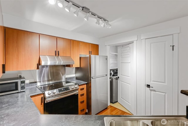 kitchen featuring stainless steel appliances, washer / clothes dryer, brown cabinetry, and under cabinet range hood