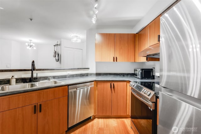 kitchen with stainless steel appliances, dark countertops, light wood-style floors, a sink, and under cabinet range hood