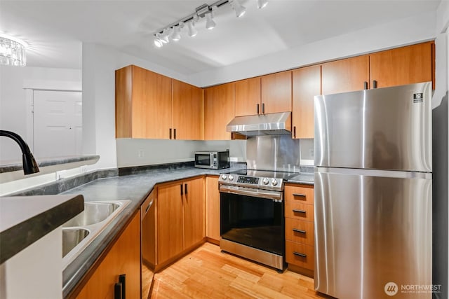 kitchen featuring light wood-style floors, dark countertops, appliances with stainless steel finishes, under cabinet range hood, and a sink