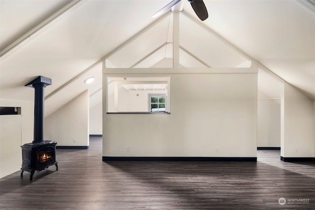 additional living space with ceiling fan, vaulted ceiling, a wood stove, and dark hardwood / wood-style floors