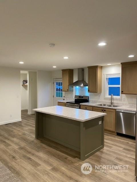 kitchen featuring sink, a center island, light wood-type flooring, wall chimney range hood, and appliances with stainless steel finishes