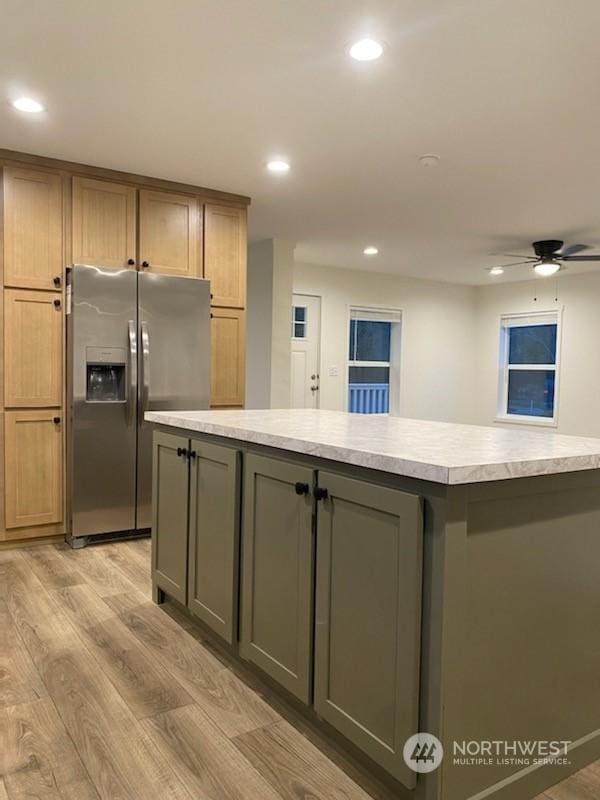 kitchen featuring stainless steel refrigerator with ice dispenser, a kitchen island, ceiling fan, and light wood-type flooring