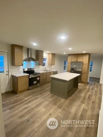 kitchen with wall chimney exhaust hood, hardwood / wood-style floors, a kitchen island, appliances with stainless steel finishes, and sink