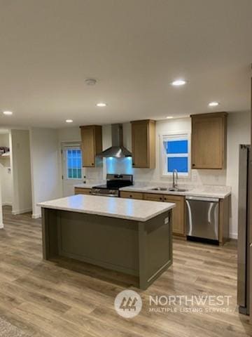 kitchen featuring stainless steel appliances, sink, wall chimney exhaust hood, light wood-type flooring, and a kitchen island