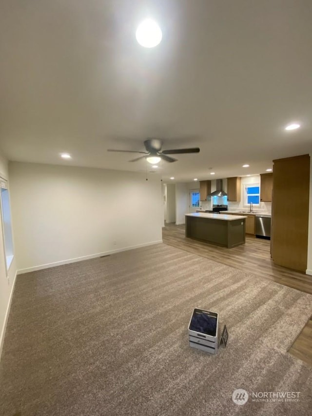 unfurnished living room featuring carpet floors, ceiling fan, and sink