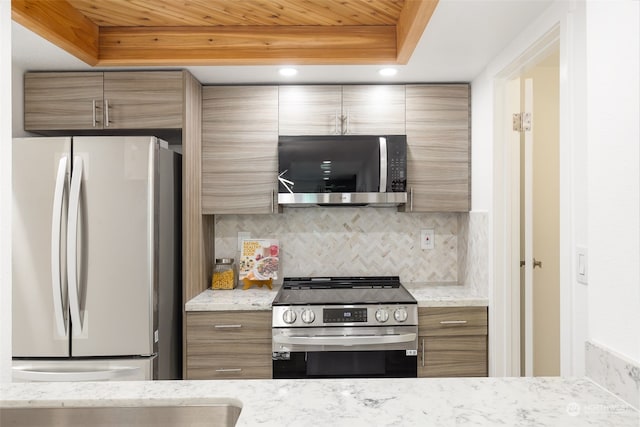 kitchen with stainless steel appliances, a raised ceiling, light stone countertops, and tasteful backsplash