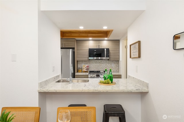 kitchen with a kitchen breakfast bar, appliances with stainless steel finishes, light stone countertops, sink, and backsplash