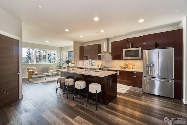 kitchen featuring a breakfast bar, a sink, wall chimney range hood, stainless steel appliances, and light countertops