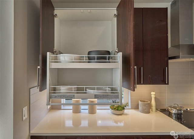 interior space with decorative backsplash, dark brown cabinets, light countertops, and wall chimney exhaust hood