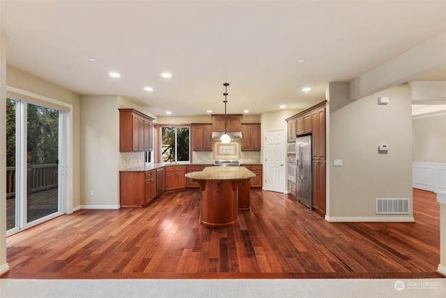 kitchen featuring pendant lighting, a center island, decorative backsplash, plenty of natural light, and light stone counters