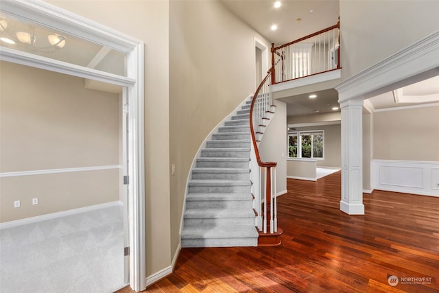 stairway with wood-type flooring, ornamental molding, and decorative columns