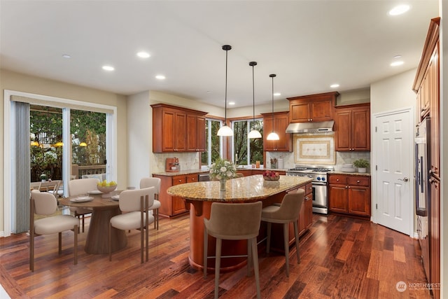 kitchen featuring dark hardwood / wood-style floors, a center island, pendant lighting, stainless steel range, and light stone counters