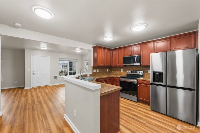 kitchen with light hardwood / wood-style floors, stainless steel appliances, kitchen peninsula, sink, and tasteful backsplash