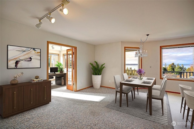 dining space featuring track lighting, light carpet, and a chandelier