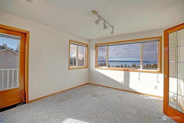 spare room featuring rail lighting, carpet floors, and a water view