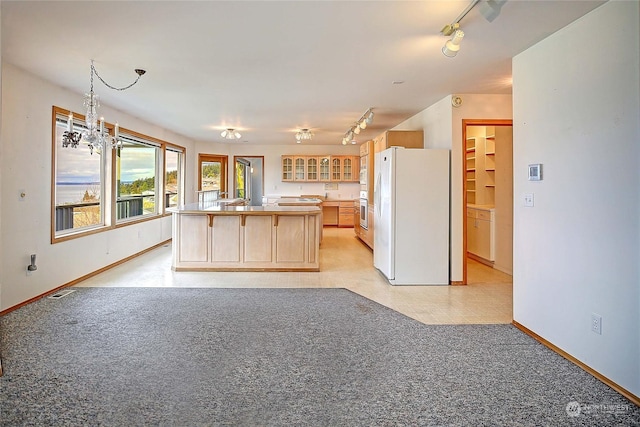 kitchen featuring light brown cabinetry, a notable chandelier, a kitchen island, white refrigerator, and light carpet