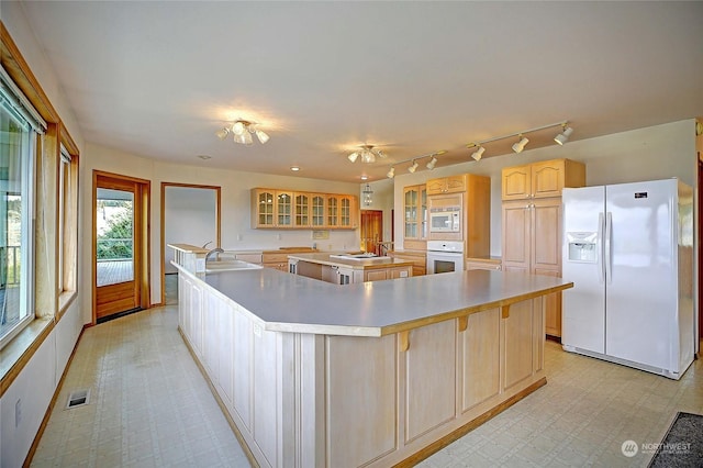 kitchen with white appliances, a large island with sink, sink, and light brown cabinets