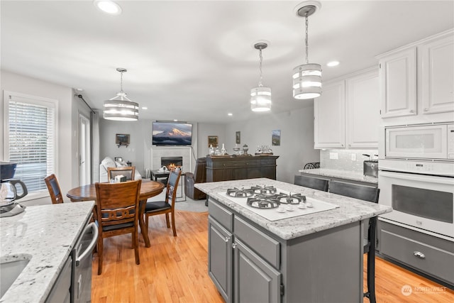 kitchen featuring a center island, white appliances, white cabinetry, hanging light fixtures, and decorative backsplash