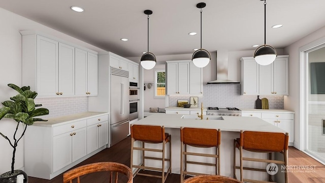 kitchen with a center island with sink, wall chimney range hood, tasteful backsplash, white cabinetry, and sink