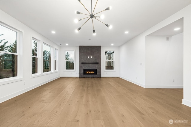 unfurnished living room featuring a fireplace, an inviting chandelier, and light hardwood / wood-style flooring