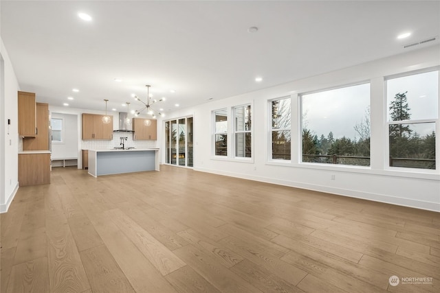 unfurnished living room with a notable chandelier, light hardwood / wood-style flooring, and sink