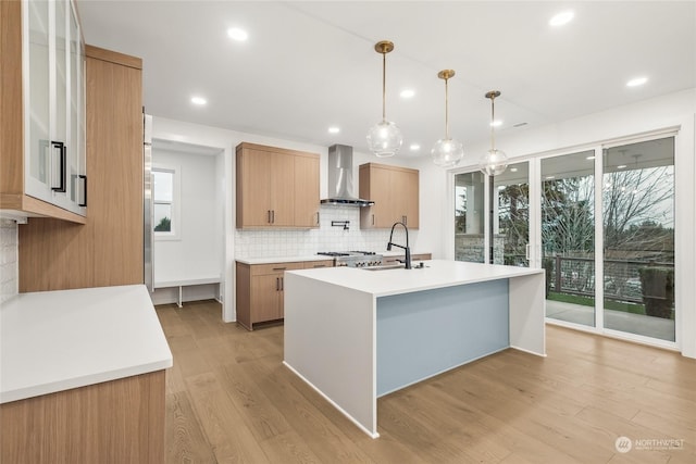 kitchen with sink, decorative light fixtures, a center island with sink, wall chimney range hood, and plenty of natural light