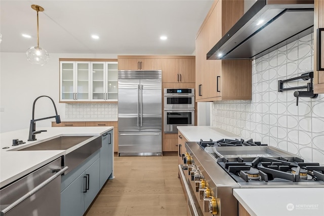 kitchen featuring premium appliances, decorative light fixtures, wall chimney range hood, decorative backsplash, and sink