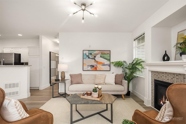 living room with a tiled fireplace, an inviting chandelier, and light hardwood / wood-style floors