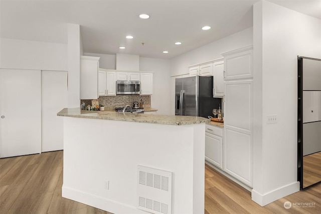 kitchen featuring tasteful backsplash, white cabinetry, light hardwood / wood-style flooring, light stone countertops, and stainless steel appliances