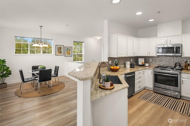 kitchen featuring pendant lighting, kitchen peninsula, white cabinetry, light stone countertops, and stainless steel appliances