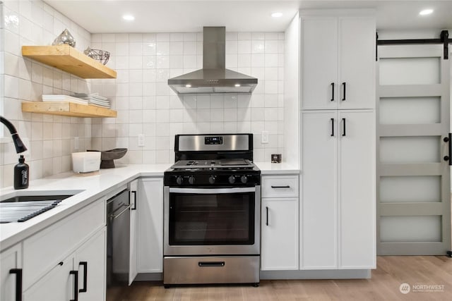 kitchen with white cabinets, sink, wall chimney range hood, and stainless steel gas range