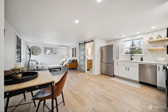 kitchen with a barn door, decorative backsplash, sink, appliances with stainless steel finishes, and white cabinets