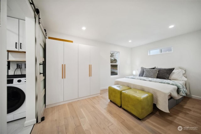 bedroom with light hardwood / wood-style floors, washer / dryer, and a barn door