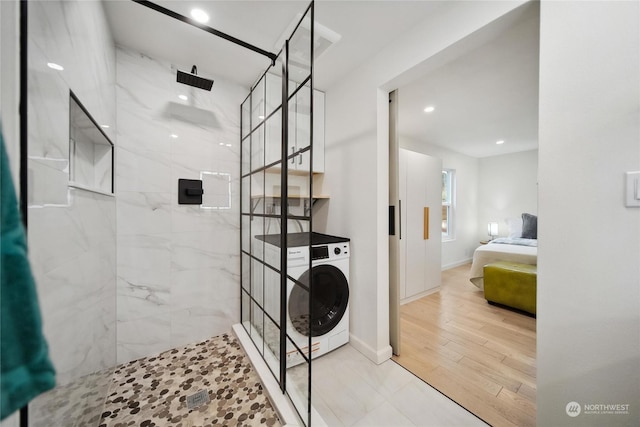 bathroom featuring wood-type flooring, tiled shower, and washer / dryer