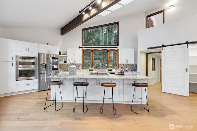 kitchen with appliances with stainless steel finishes, white cabinetry, a center island, light stone countertops, and a barn door