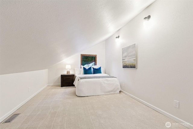 bedroom with vaulted ceiling, light colored carpet, and a textured ceiling