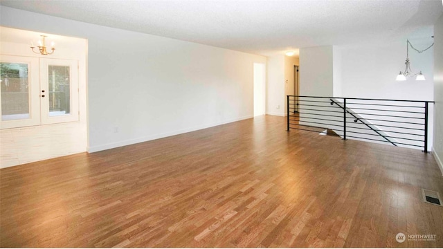 unfurnished room with french doors, an inviting chandelier, a textured ceiling, and hardwood / wood-style flooring