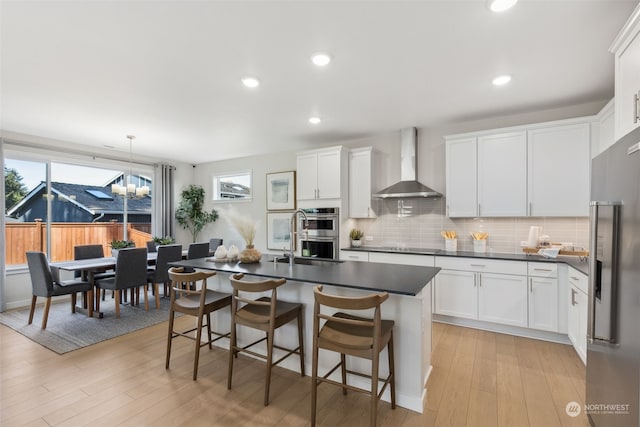 kitchen featuring stainless steel appliances, wall chimney exhaust hood, white cabinetry, and hanging light fixtures